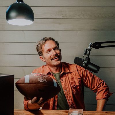 image6 Man holds football in his podcast room in front of maple wood wall.